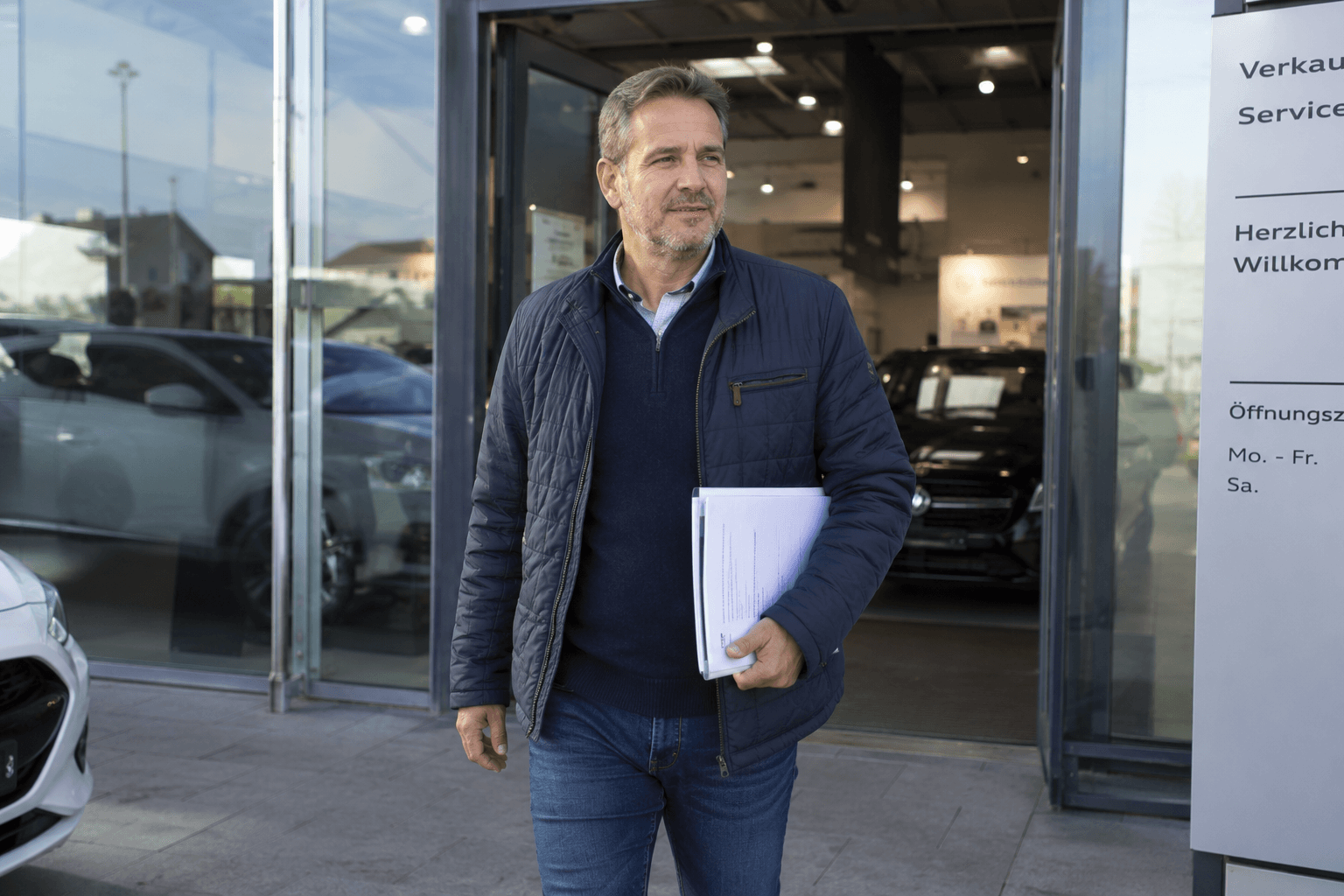 Mann läuft mit Dokumenten unter dem Arm auf dem Autohaus