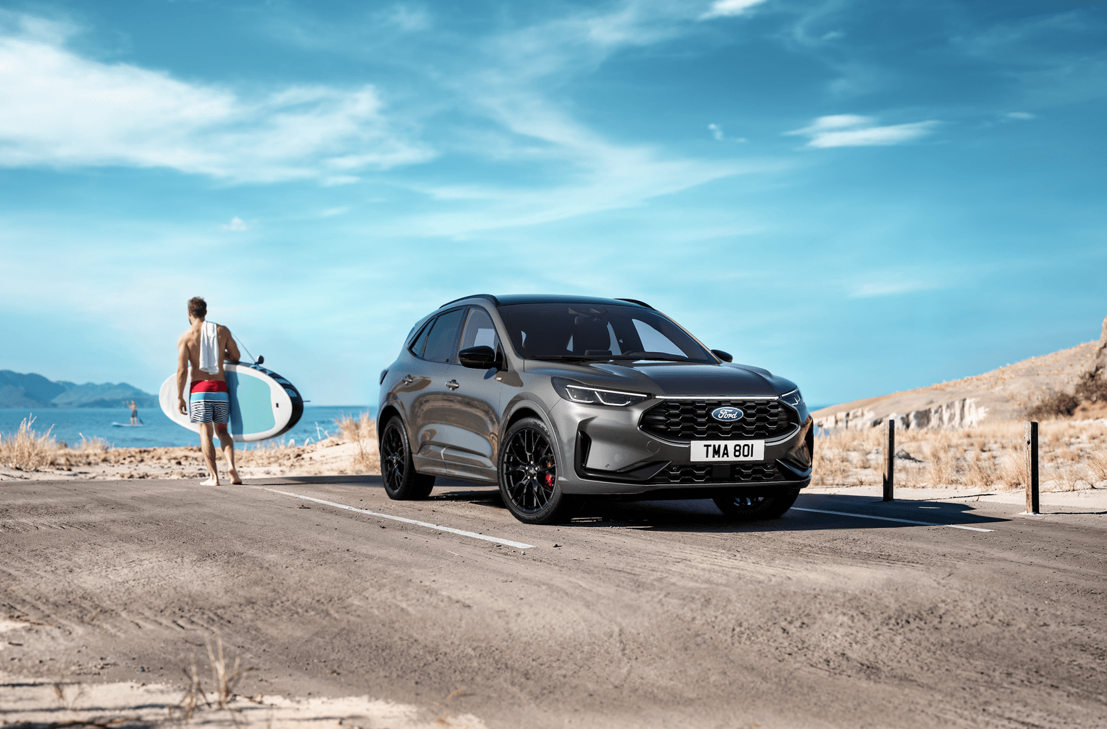 Ford PKW in der Vorderansicht, mit einem Mann, der ein Surfbrett trägt, im Hintergrund am Strand