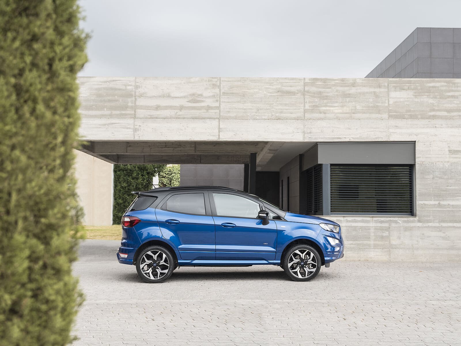 Seitenansicht eines blauen Ford Eco Sport PKW vor einem modernen Gebäude mit grauer Fassade