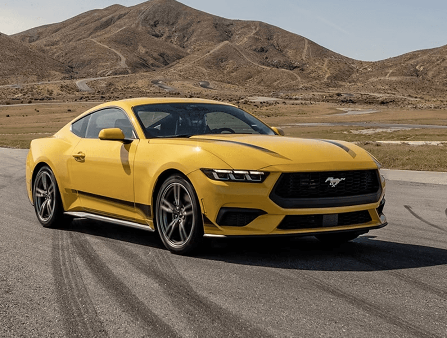 Ford Mustang in Gelb, Seitenansicht auf einer Straße mit Bergen im Hintergrund
