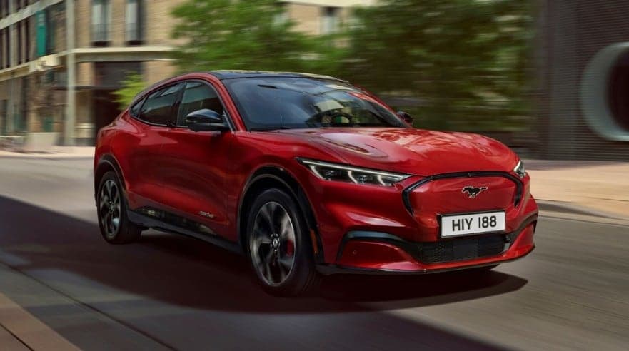 Ford Mustang Mach e in Rot, Vorderansicht, auf einer urbanen Straße mit modernen Gebäuden im Hintergrund